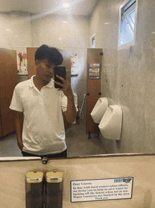 a man taking a selfie in a public restroom with a sign that says every drop