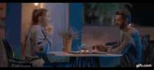 a man and a woman are sitting at a table holding hands and looking at each other .