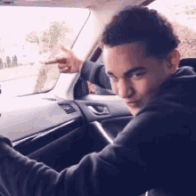 a young man is sitting in the driver 's seat of a car and pointing at something .