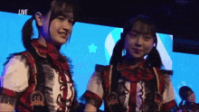two girls are standing next to each other in front of a large screen that says live