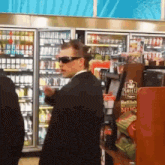a man wearing sunglasses stands in front of a shelf that says sweetz