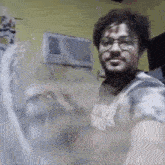 a man wearing glasses and a tie dye shirt is taking a selfie in front of a window air conditioner .