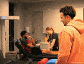 a man in an orange hoodie stands next to a man in a chair