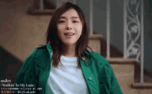 a woman in a green jacket stands in front of a set of stairs with the words milet walkin ' in my lane