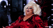 a drag queen is wearing a red dress and wig and is laughing