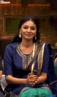 a woman in a blue and gold dress is sitting with her hands folded .