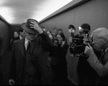a man in a suit and hat is being photographed by a cameraman