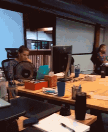 a woman sits at a desk with a fan and a dell monitor