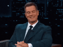 a man in a suit and tie smiles while sitting in a chair