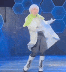 a woman in a white coat and green scarf is dancing on a stage