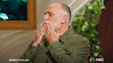 a man with a beard is covering his mouth with his hands and the nbc logo can be seen in the corner