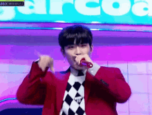a man in a red jacket is singing into a microphone