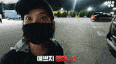a woman wearing a black mask is standing in a parking lot with a yellow van in the background
