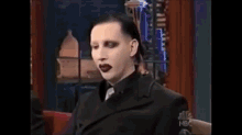 a man in a black suit and tie is making a funny face with his tongue out .