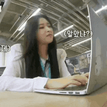 a woman is sitting at a table using a laptop computer with korean writing on the screen .