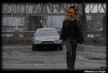 a man with a mask on his face is walking in front of a car with maleficus origin written on the bottom