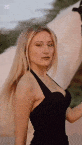 a beautiful blonde woman in a black dress is standing in front of a white tent .