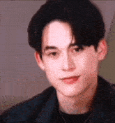 a close up of a young man 's face wearing a black jacket and a necklace .