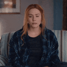 a woman with red hair and a plaid shirt is sitting on a couch with her eyes closed