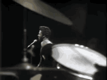 a man is singing into a microphone while playing drums in a black and white photo .