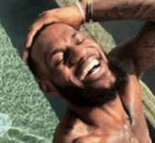 a shirtless man with a beard is laughing and holding his head in a pool .