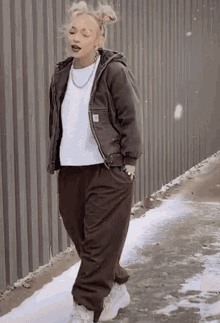 a woman wearing a brown jacket and brown pants is standing on a sidewalk in the snow .