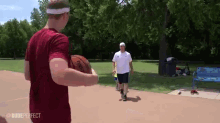 a man in a red shirt is holding a spalding basketball while another man looks on .