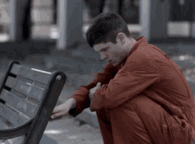 a man in a red jumpsuit is squatting on a bench