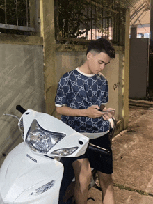 a young man leans on a white honda scooter
