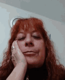 a woman with red hair is making a funny face with her hand on her chin .