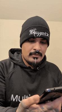 a man wearing a black beanie that says blazzard looks at his phone