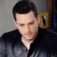 a man in a black shirt is looking down at something while sitting in a kitchen .