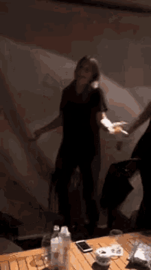 a woman in a black shirt is dancing in a dark room next to a table