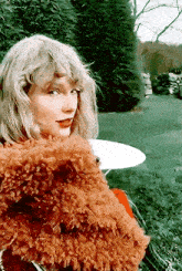 taylor swift is wearing a fur coat and holding a teddy bear in her lap .