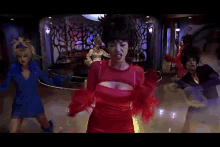 a group of women are dancing in a room with a woman in a red top holding a blue object .