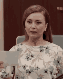 a woman in a floral top holds a piece of paper