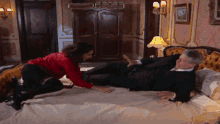 a man in a suit is laying on a bed while a woman in a red shirt touches his feet