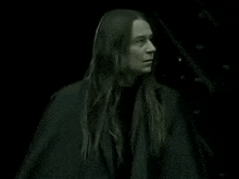 a man with long hair wearing a black coat