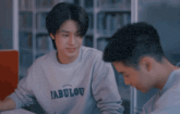 two young men are sitting at a table and one of them has a finally plus shirt on