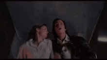 a man and a woman are standing next to each other in a dark room looking up at the sky .