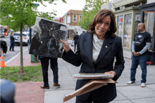 a woman in a black suit is holding a picture of a man in a black shirt