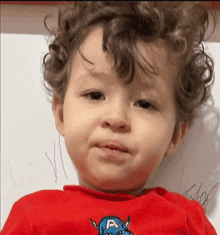 a little boy with curly hair is wearing a red shirt with a picture of captain america