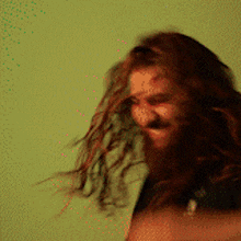a man with long hair and a beard is smiling with his hair blowing in the wind