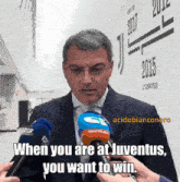 a man in a suit is talking into a microphone with the words when you are at juventus you want to win on the bottom