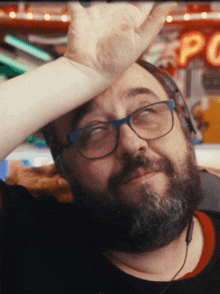 a man wearing glasses and headphones wipes his forehead with his hand