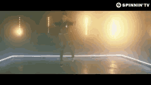 a man is dancing in a dark room in front of a screen that says spinnin ' tv .