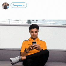 a man in a dell shirt sits on a couch looking at a phone