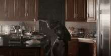 a man in a black jacket is standing in a kitchen looking at plates on the counter .
