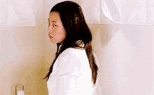 a woman in a white robe is standing in a bathroom looking at the camera .