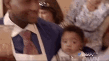 a man in a suit and tie is holding a baby in his lap .